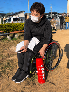 地域防災訓練で、車椅子利用者が消火器の使用方法を確認する様子